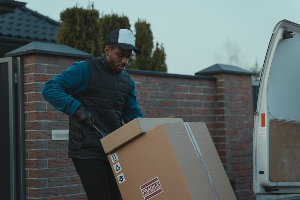A mover lifting a large box marked fragile out to the van outside a house
