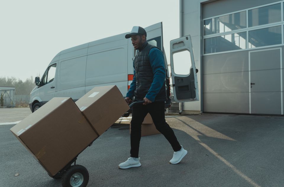 A mover wheeling a loaded hand truck of boxes across to the van
